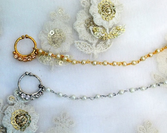 May include: Two gold nose rings with chains attached. The chains are made of small white beads and gold links. The nose rings are decorated with clear rhinestones.