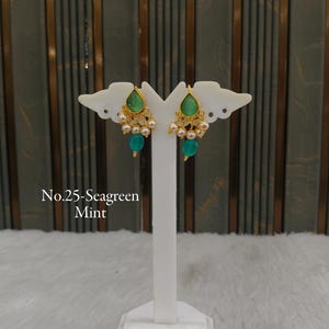 May include: A pair of gold-toned earrings featuring a teardrop-shaped sea green mint stone at the top, accented with small white pearls and a dangling round sea green mint bead. The text No.25- Sea green Mint is visible in the image.