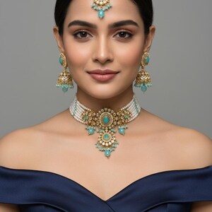 May include: An ornate gold-toned jewelry set featuring turquoise-colored stones and white pearls. The set includes a necklace, earrings, and a headpiece. The necklace has a central pendant with a floral design. The earrings are bell-shaped.
