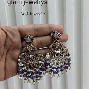 Peut inclure: Une paire de boucles d'oreilles pendantes avec une finition dorée. Les boucles d'oreilles présentent un motif rond orné de pierres noires et blanches. Les boucles d'oreilles sont rehaussées d'une couche de perles blanches et d'une couche de perles violettes.