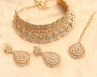 May include: A rose gold bridal jewellery set featuring a choker necklace, earrings, and a maang tikka. The set is embellished with sparkling white stones.