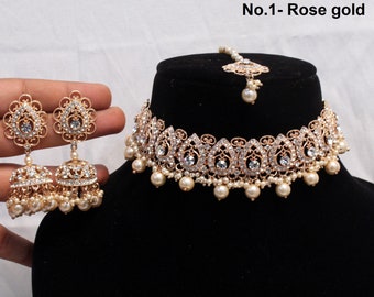 May include: A rose gold bridal jewellery set comprising a choker necklace, earrings, and a headpiece. The necklace and earrings feature a floral design with clear crystals and faux pearls. The headpiece has a central pearl drop.
