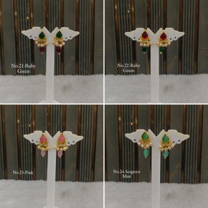 May include: Four pairs of gold-toned drop earrings displayed on white stands. Each pair features a teardrop-shaped stone in green, ruby, pink, or seagreen, accented with small white beads and gold filigree details. Text labels identify each set.