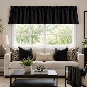 May include: A solid black window valance featuring a rod pocket top and a gathered, ruffled header. The fabric is opaque and hangs in uniform vertical folds across the width of the window, providing a clean, straight-edged bottom hem.