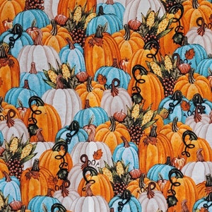 Może przedstawiać: Powtarzający się wzór dyni w odcieniach pomarańczu, bieli i turkusu. Dynie mają kręcone pędy i są przeplatane kolbami kukurydzy. Ogólnym motywem jest jesień i żniwa.