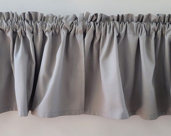Pode incluir: Uma valance cinzenta com babados e uma borda superior franzida. A valance é feita de um tecido macio e leve e tem um design simples e elegante.