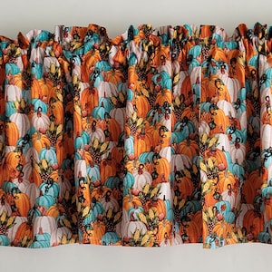 May include: A valance featuring a repeating pattern of pumpkins in shades of orange, teal, and white. The fabric is gathered at the top, creating a ruffled effect. The design evokes a fall or harvest theme.