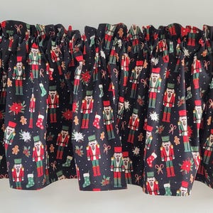 May include: A black valance with a repeating pattern of red, green, and white Christmas-themed images, including nutcrackers, gingerbread men, and snowflakes. The valance is gathered at the top.