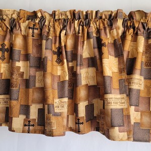 May include: A brown and beige valance with a patchwork design featuring crosses and religious text. The valance has a gathered ruffle at the top.