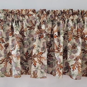 May include: A valance with a brown, green, and white pattern of leaves and pine cones. The valance is made of a soft, woven fabric.