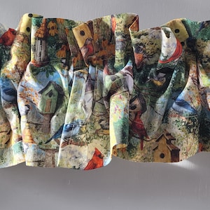 May include: A colourful fabric valance with a bird and birdhouse pattern. The valance is made of a white fabric with a green, yellow, and red pattern. The valance is ruffled and has a gathered look.