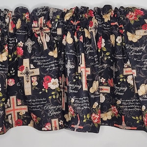 May include: A black fabric valance with a repeating pattern of crosses, flowers, and butterflies. The design includes the words "Amazing Grace" in script. The flowers are red and white, and the crosses have a red and beige color scheme.