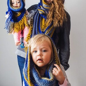 Pode incluir: Duas crian&ccedil;as usando cachec&oacute;is de croch&ecirc; azul, amarelo e cinza com franjas. Os cachec&oacute;is s&atilde;o usados como capuzes. As crian&ccedil;as est&atilde;o sorrindo.