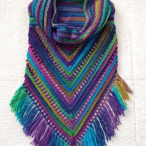 Pode incluir: Um xale de croch&ecirc; colorido com uma borda de franjas. O xale &eacute; feito em tons de roxo, azul, verde e marrom.