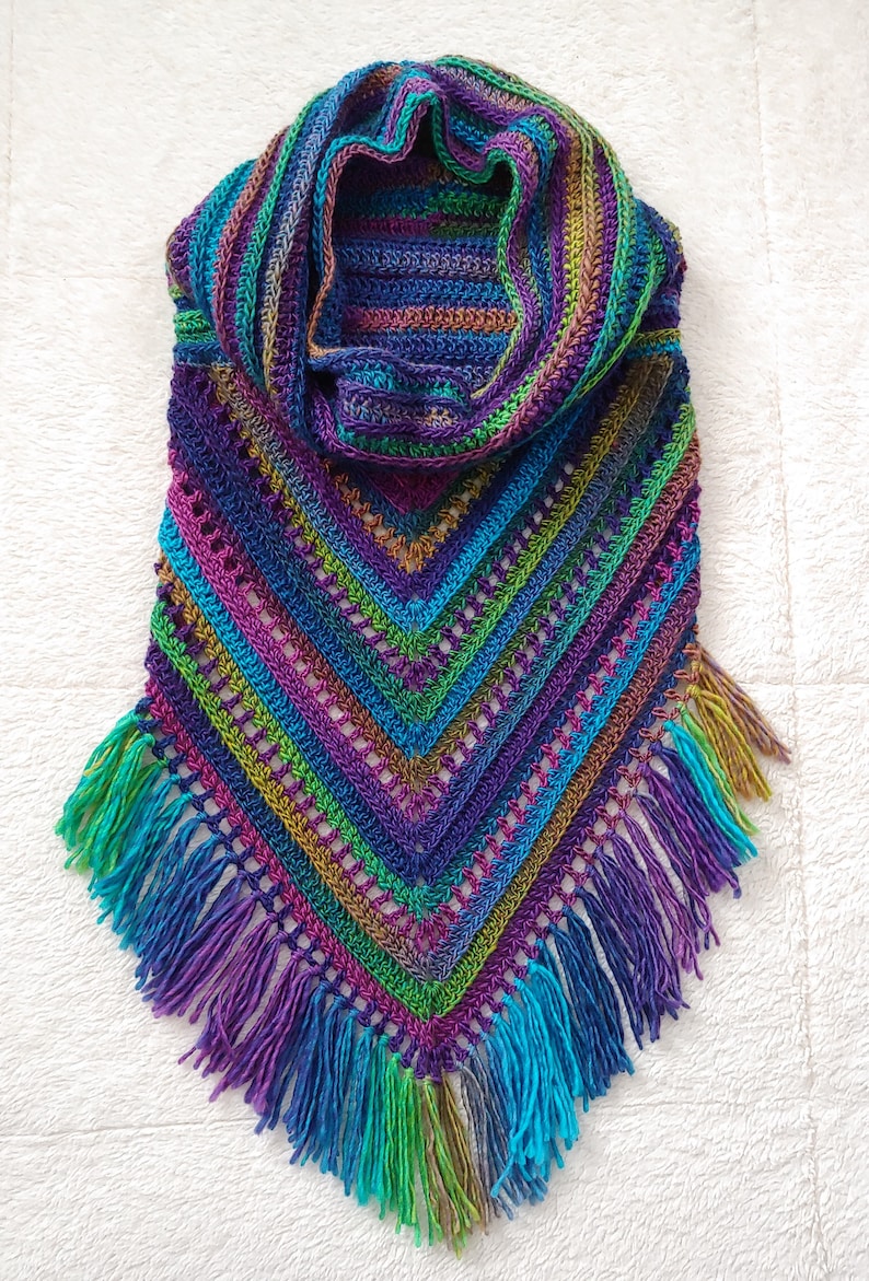 Pode incluir: Um xale de croch&ecirc; colorido com uma borda de franjas. O xale &eacute; feito em tons de roxo, azul, verde e marrom.