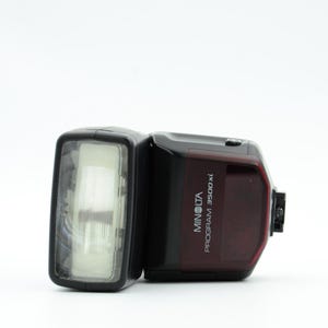 Op de afbeelding: Een zwarte en rode Minolta Program 3500xl flitser. De flitser heeft een rechthoekige kop met een doorzichtige voorkant en een rode achterkant met witte tekst. De flitser is ontworpen voor gebruik met camera's.