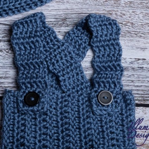 May include: Blue knitted baby overalls with black buttons. The overalls have a criss-cross strap design in the back.