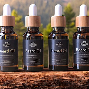 May include: Four 30 ml amber glass bottles with bamboo lids and droppers. Each bottle contains beard oil and has a black label with the text "SHANTI naturals Beard Oil" and a list of ingredients. The bottles are arranged in a row on a wooden surface.