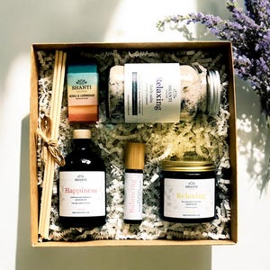 Könnte beinhalten: Eine braune Geschenkbox gefüllt mit Bad- und Körperpflegeprodukten. Die Box enthält ein Glas mit Badesalz mit der Aufschrift "Relaxing", eine Flasche mit ätherischem Öl mit der Aufschrift "Balancing", eine Flasche mit Raumspray mit der Aufschrift "Happiness", eine Kerze mit der Aufschrift "Relaxing" und ein Set mit Schilfrohrdiffusoren. Die Produkte stammen alle von der Marke "SHANTI Naturals."