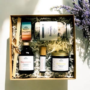 Könnte beinhalten: Eine Geschenkbox gefüllt mit Selbstpflegeartikeln, darunter ein Glas mit Badesalz mit der Aufschrift "Relaxing", eine Kerze mit der Aufschrift "Relaxing", eine Flasche ätherisches Öl mit der Aufschrift "Balancing", eine Flasche Diffusionsöl mit der Aufschrift "Happiness" und eine Seife mit der Aufschrift "Shanti" mit einem Regenbogenmuster.