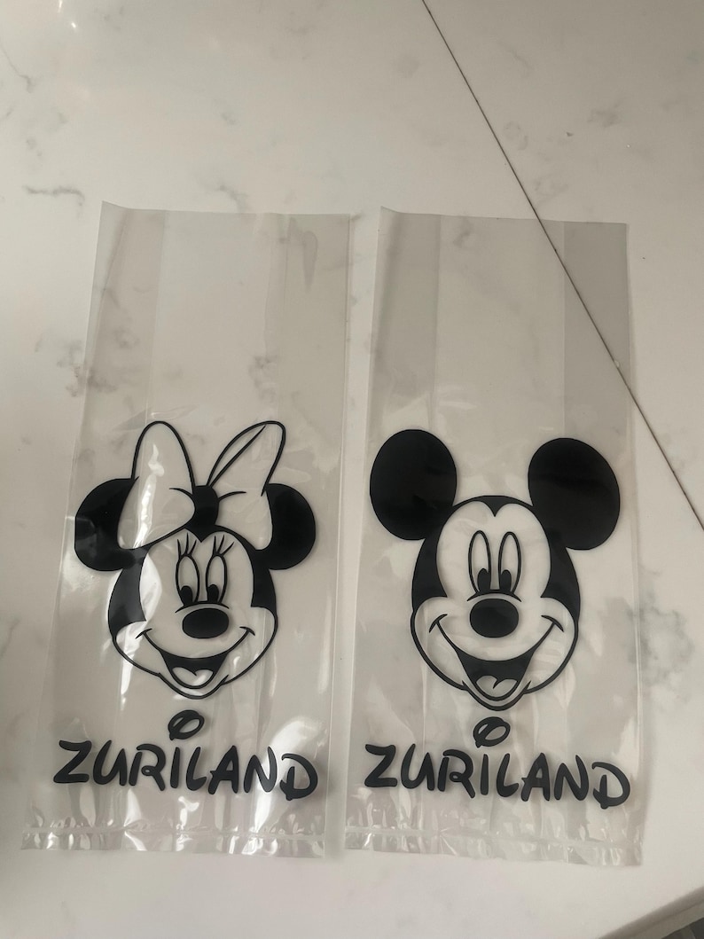 May include: Two clear plastic bags featuring black and white cartoon character faces. One bag has Minnie Mouse, the other has Mickey Mouse. The word "ZURILAND" is printed in black at the bottom of each bag.