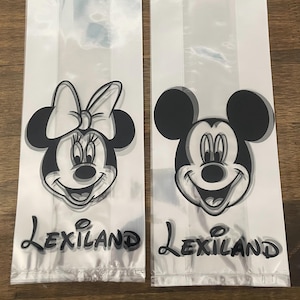 May include: Two clear plastic treat bags featuring Mickey and Minnie Mouse. The black and white illustrations of the iconic characters are printed on the front of the bags. The word "Lexiland" is printed in a script font below the characters.