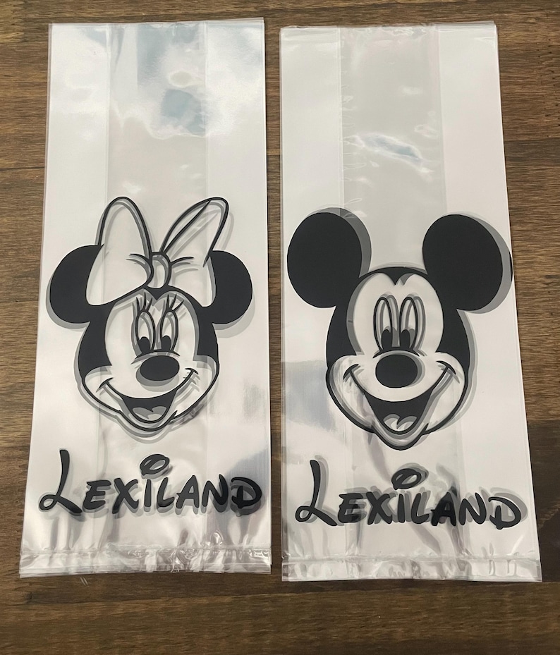 May include: Two clear plastic treat bags featuring Mickey and Minnie Mouse. The black and white illustrations of the iconic characters are printed on the front of the bags. The word "Lexiland" is printed in a script font below the characters.