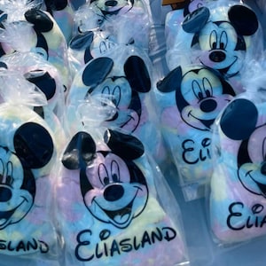 May include: A collection of clear plastic bags filled with colorful cotton candy. Each bag features a smiling Mickey Mouse face and the name "Eliasland" in black text. The cotton candy has pastel colors.