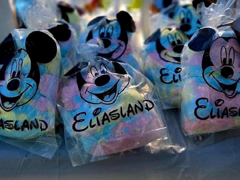 May include: Several clear plastic bags filled with colorful cotton candy. Each bag features a Mickey Mouse design and the text "Eliasland". The cotton candy is a mix of blue, pink, and yellow.