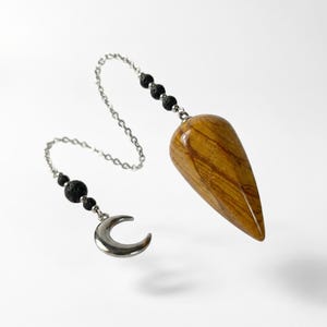 May include: A teardrop-shaped brown and tan wood-grain pendulum attached to a silver-toned metal chain. The chain features three small black porous beads near the pendulum and two near a polished silver-toned crescent moon charm at the end.