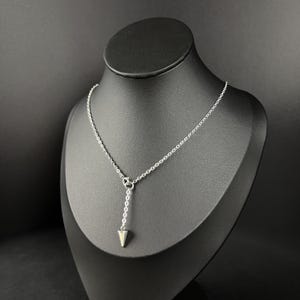 Op de afbeelding: Een zilveren ketting met een puntige hanger. De ketting wordt getoond op een zwart manekin.