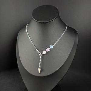 Peut inclure: Un collier en chaîne argent avec un pendentif en forme de cône argenté. Le collier comporte trois perles en forme d'étoile dans les tons bleu, rose et blanc.