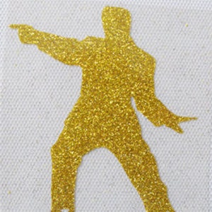 May include: Gold glitter silhouette of a person in a dancing pose with one arm outstretched and the other arm bent at the elbow.