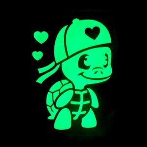 Op de afbeelding: Een gloeiende groene cartoon schildpad met een pet met een hart en twee zwevende harten. De schildpad heeft een lachend gezicht en een schildpatroon. De afbeelding staat tegen een zwarte achtergrond.