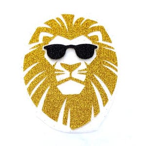 May include: A gold glitter lion head with black sunglasses. The lion's mane is detailed and the sunglasses are a classic style.