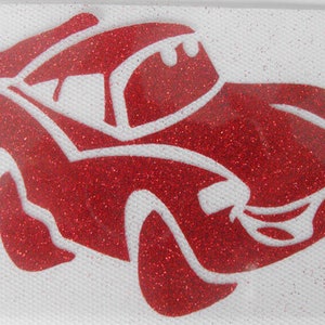 May include: A red glitter car design with white accents. The car has a stylized, cartoonish appearance, with details like a windshield, wheels, and a smiling face. The design is set against a white background.