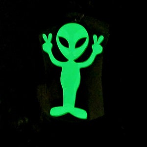 May include: A green glow-in-the-dark alien figure with peace signs for hands.