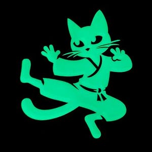 Peut inclure: Une silhouette verte d'un chat en position de karaté, avec une jambe levée et l'autre jambe au sol. Le chat porte un uniforme de karaté avec une ceinture.