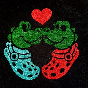 Könnte beinhalten: Zwei grüne Glitzerkrokodile mit roten Glitzer-Schuhen stehen sich gegenüber, zwischen ihnen ein rotes Glitzerherz.