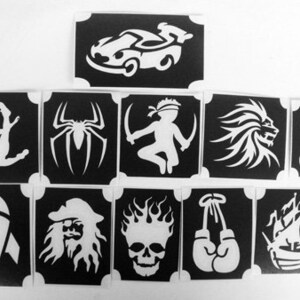 May include: A collection of black and white stencils featuring various designs. Included are a race car, spider, soccer player, ninja, lion, dragon, rocket, pirate, skull, boxing gloves, and a sailboat.