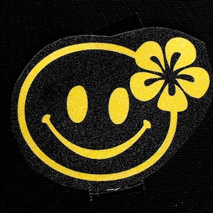 Könnte beinhalten: Ein gelbes Smiley-Gesicht mit einer Blume obenauf, auf schwarzem Hintergrund.
