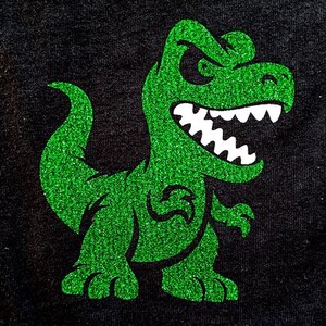 May include: Green glitter dinosaur with a toothy grin on a black background.