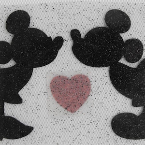 Puede incluir: Dos figuras de silueta negra de Mickey Mouse y Minnie Mouse besándose con un corazón rosa en el medio.