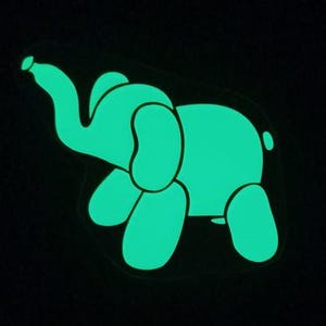 Könnte beinhalten: Ein leuchtend grüner, im Dunkeln leuchtender Elefantenaufkleber. Der Elefant blickt nach links und hat seinen Rüssel erhoben.