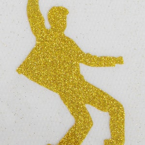 May include: A gold glitter silhouette of a person dancing. The silhouette is cut out and ready to be used for crafting projects.