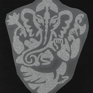May include: A white, glittery iron-on patch depicting a detailed illustration of the Hindu deity Ganesha. The image shows Ganesha with his elephant head, trunk, and four arms, holding various objects. The patch is designed for use on clothing or other fabric items.