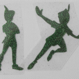 May include: Four green glitter silhouette cutouts of Peter Pan, a classic Disney character. The cutouts are in various poses, including flying and standing.