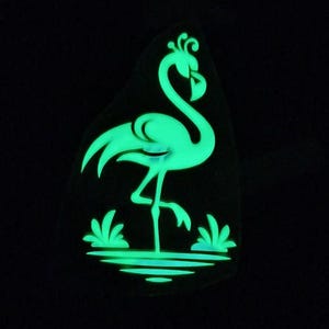 May include: A glowing green flamingo silhouette on a dark background. The flamingo is standing in water with stylized plants. The image has a neon effect, with the flamingo and water elements emitting a bright green light.