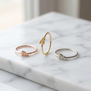 May include: Three thin metal rings, each featuring a small charm shaped like a wedge of Swiss cheese with visible holes. One ring is rose gold, one is yellow gold, and one is silver, all displayed together as a set of delicate jewelry pieces.