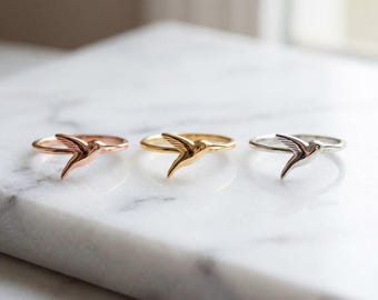 May include: Three thin metal rings, each featuring a small hummingbird motif. The rings are finished in rose gold, yellow gold, and silver tones, respectively. Each band is smooth and circular, with the bird design extending from the top.